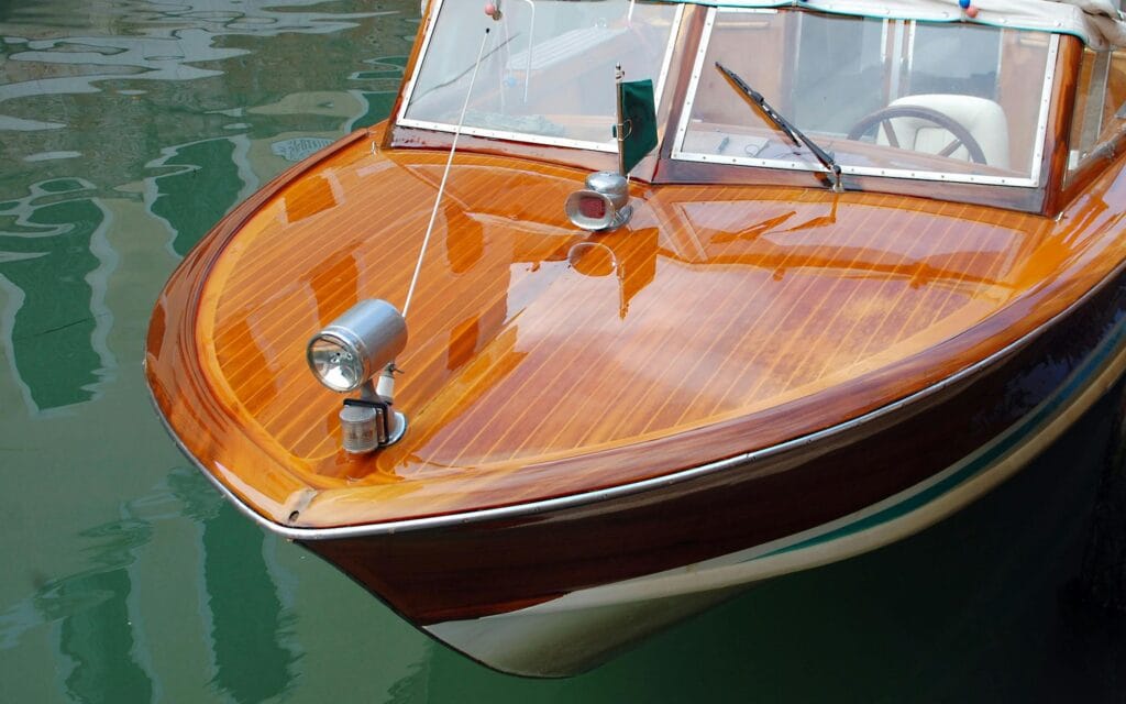 Close-up of an elegant wooden speedboat reflecting on calm water.